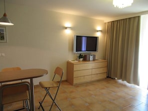 A compact living space with a flat-screen TV mounted on the wall, a wooden cabinet below, and a dining area with a table and chairs. - Holiday apartment on the Csopak promenade (Csopak)
