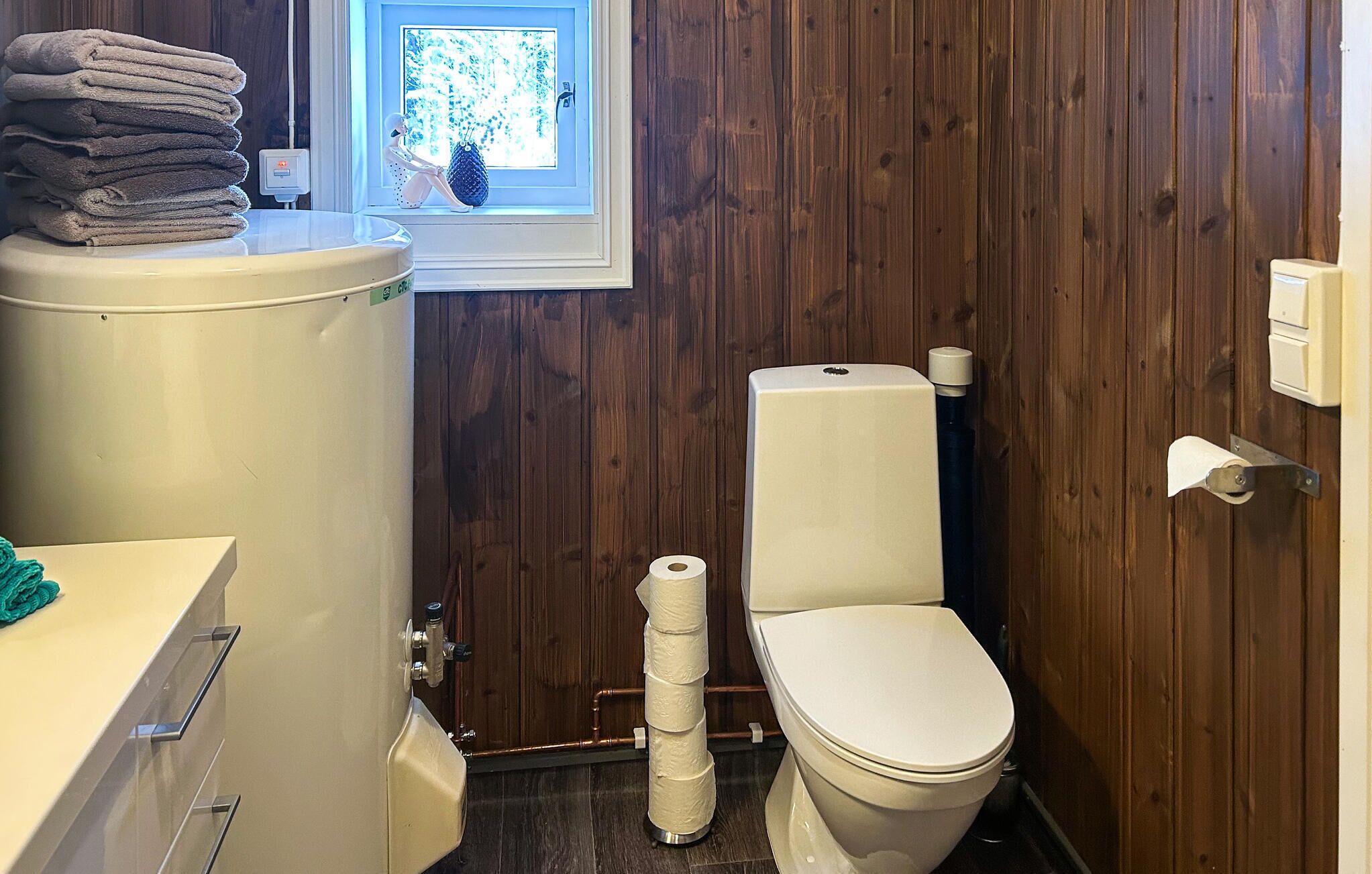 Une salle de bain avec des toilettes, une pile d’serviettes et une fenêtre donnant sur des arbres.