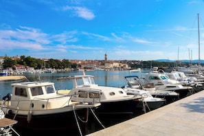 A marina with several boats docked, a clear sky, and a distant view of a town with a prominent tower. - Holiday Apartment RESIDENCE JELICA 2 (Krk)