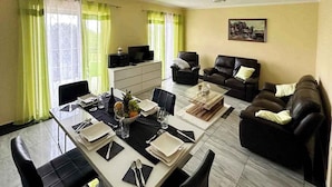 Ein Essbereich mit einem Tisch für vier Personen, zwei Sofas und einem Fernseher im Hintergrund.