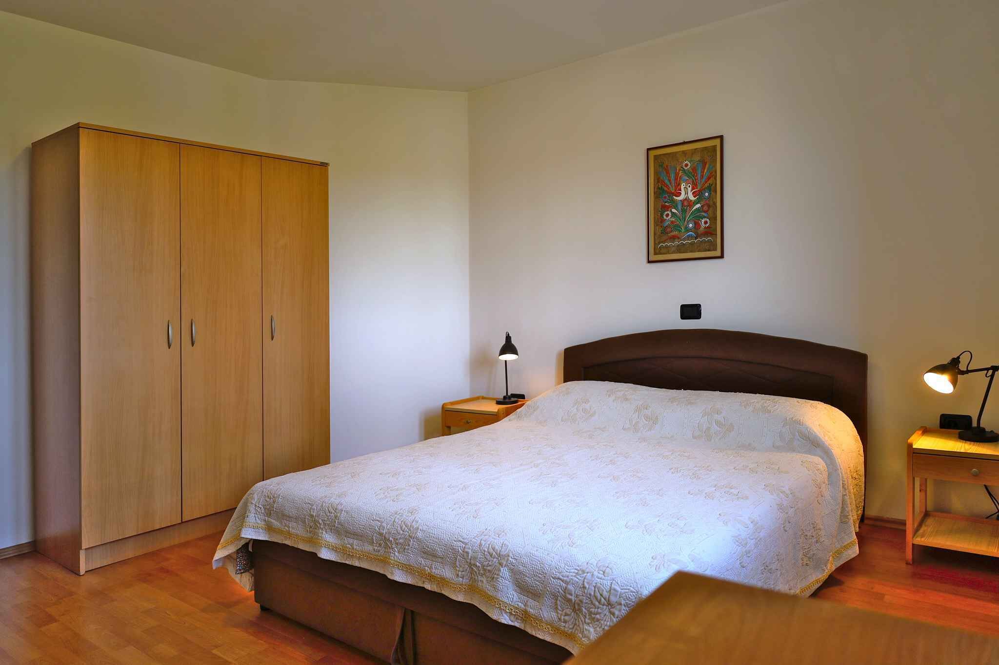 A bedroom with a bed, a wardrobe, a nightstand, a lamp, and a painting on the wall.