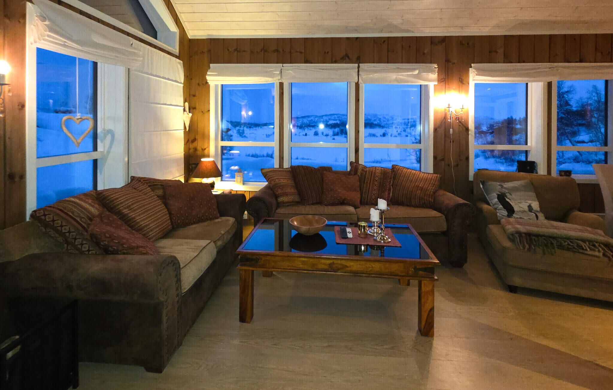 Een gezellige woonkamer met houten details, grote ramen en uitzicht op een besneeuwd landschap.