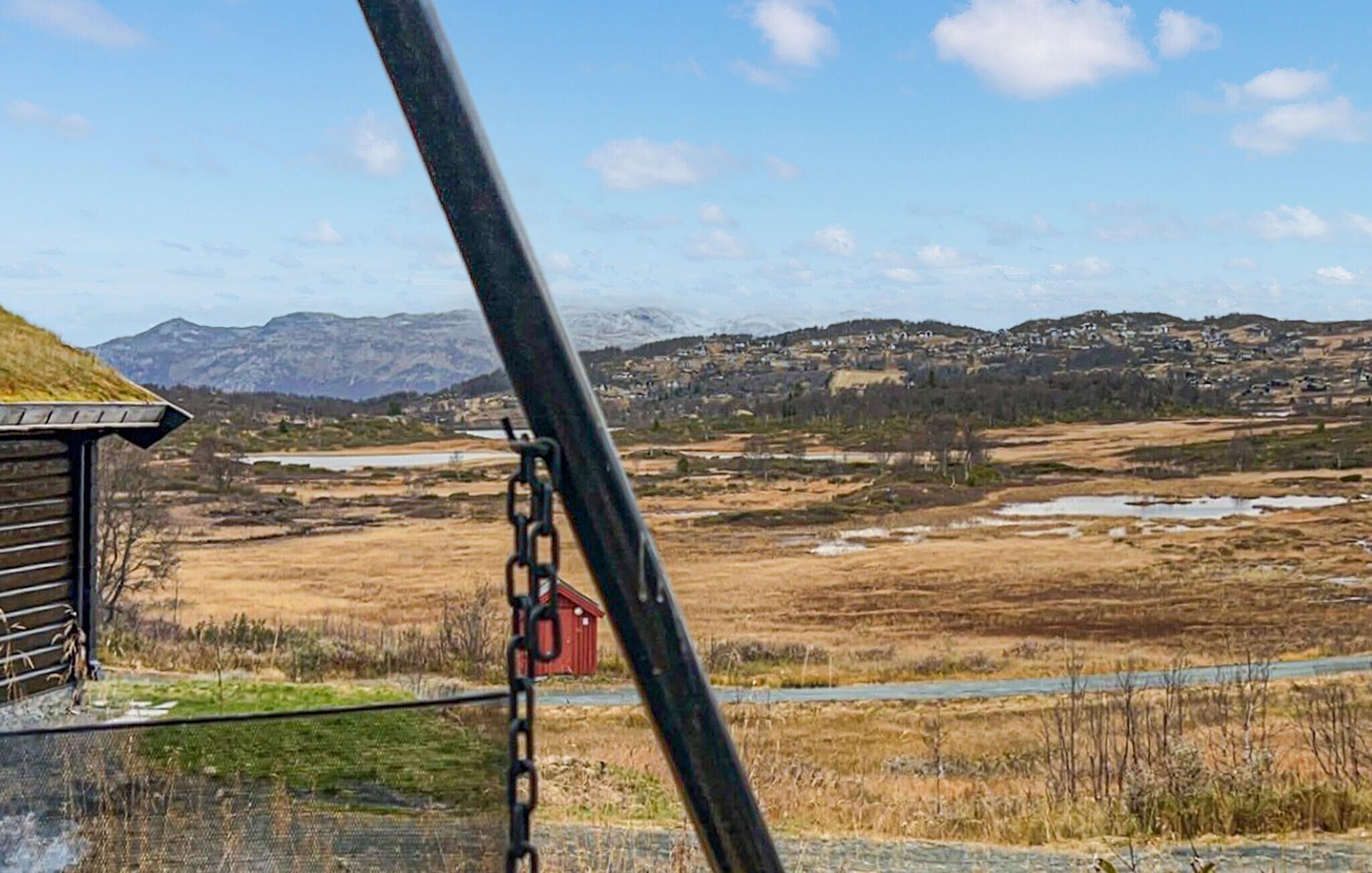 Un paysage rural avec des montagnes, un petit bâtiment et une structure rouge au loin.