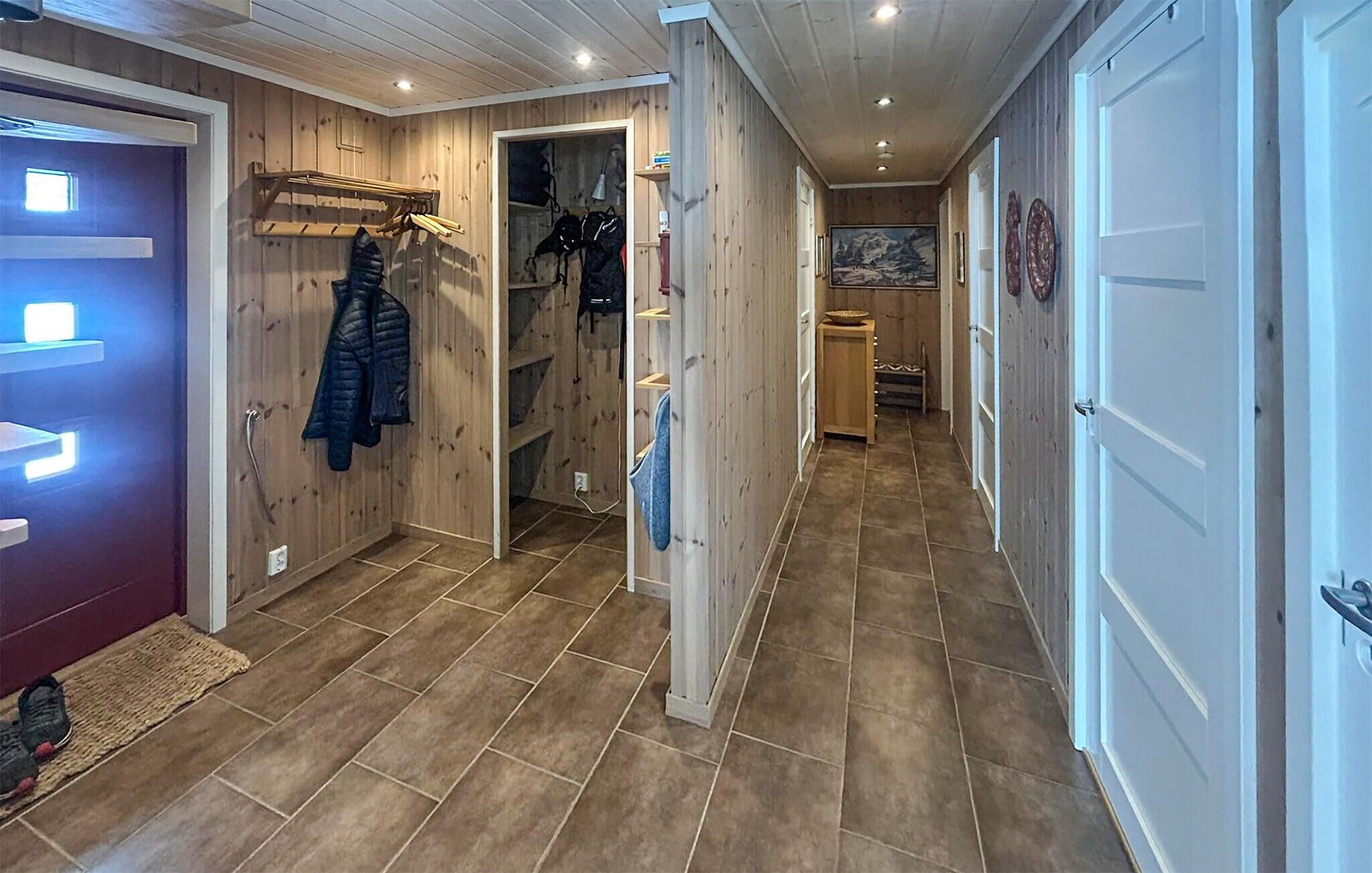A hallway with wooden walls, a coat rack, a door with a light, and a tiled floor.