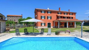 Une piscine avec des chaises longues, un patio couvert et une grande maison à la façade rouge.