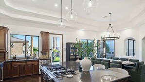 A spacious kitchen with a large island, built-in cabinets, and a dining area with green upholstered chairs. - Epic Views | Pool • Spa • RV Garage | Near Marina (Lake Havasu City)