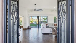 A spacious living area with a white sofa, a ceiling fan, and a view through glass doors to an outdoor patio. - Epic Views | Pool • Spa • RV Garage | Near Marina (Lake Havasu City)