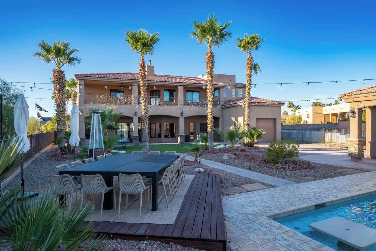 A multi-story house with a patio, outdoor seating, palm trees, and a swimming pool.