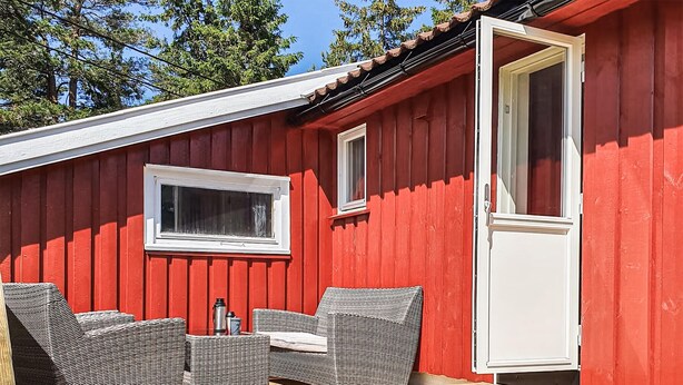 Un edificio de madera rojo con puerta y ventana blancas, amueblado con sillas de mimbre y una mesa.