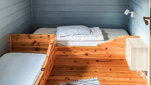Una habitación pequeña y funcional con una cama individual, un banco de madera y una mesita.