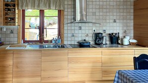 Une cuisine avec des meubles en bois, une hotte de cuisinière en acier inoxydable, une machine à café et une fenêtre donnant sur un paysage verdoyant.