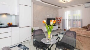 Un soggiorno moderno con un tavolo da pranzo in vetro, sedie nere, un divano beige e una TV appesa al muro.