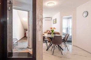 Un salón moderno con una mesa redonda de cristal, dos sillas grises, un sofá marrón y un jarrón con flores.