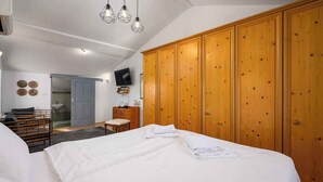 Une chambre avec un grand lit, une armoire en bois et un téléviseur fixé au mur.