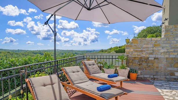 Une terrasse avec trois chaises longues, un grand parasol et un mur en pierre.