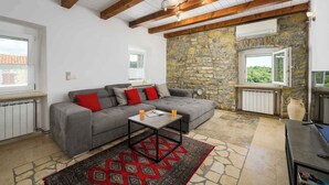 Un salon chaleureux avec un canapé gris, un tapis à motifs et un mur en pierre.