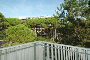 En byggnad omgiven av tät vegetation, med ett metallräcke i förgrunden.
