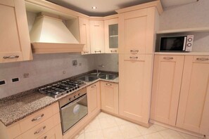 A kitchen with light-colored cabinets, a gas stove, a microwave, and a sink. - Holiday apartment with air conditioning and balcony (Lignano Sabbiadoro)