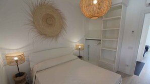 Quarto com cama, duas luminárias de cabeceira, um painel de parede tecido e um closet espaçoso.