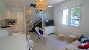 Um espaço de estar moderno com cozinha, área de jantar e escada para uma varanda.