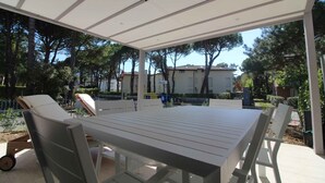 Uma área de pátio externa com mesa e cadeiras, cercada por árvores e um céu claro.