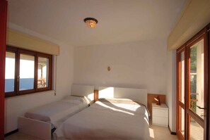 A bedroom with two beds, a nightstand, and a window with a view of the sea. - Holiday apartment with air conditioning, terrace and garden (Lignano Sabbiadoro)