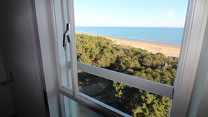 A view from a window overlooking a beach and forested area. - Holiday flat with air conditioning and balcony with sea view (Lignano Sabbiadoro)