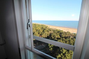 A view from a window overlooking a beach and forested area. - Holiday flat with air conditioning and balcony with sea view (Lignano Sabbiadoro)