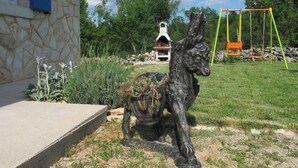 A garden with a stone wall, a statue of a deer, and a swing set. - Holiday home with garden (Malinska)