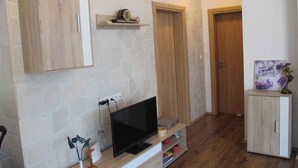 A modern living room with a flat-screen TV, wooden cabinets, and a stone-patterned wall. - Holiday home with garden (Malinska)