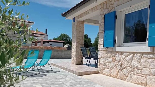 A stone building with a covered patio area, outdoor seating, and a view of neighboring houses. - Holiday home with garden (Malinska)