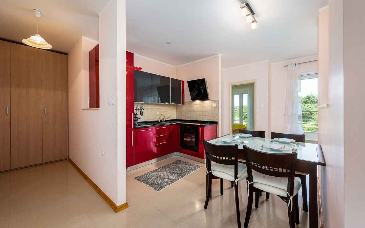 A modern kitchen with red cabinets, a black countertop, and a dining area with two chairs and a table.