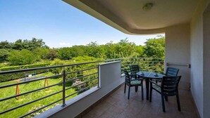 Een balkon met een tafel en stoelen, uitzicht op een groen landschap, en een metalen hekwerk.