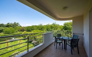 A balcony with a table and chairs, a view of a green landscape, and a metal railing. - Holiday apartment with air conditioning (Umag)