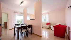 Een moderne woonkamer met een eethoek, een rode poef en een witte bank met rode kussens.