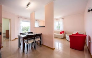A modern living room with a dining area, a red ottoman, and a white sofa with red cushions. - Holiday apartment with air conditioning (Umag)