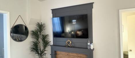 A living room with a fireplace, a flat-screen TV mounted above it, and a ceiling fan.