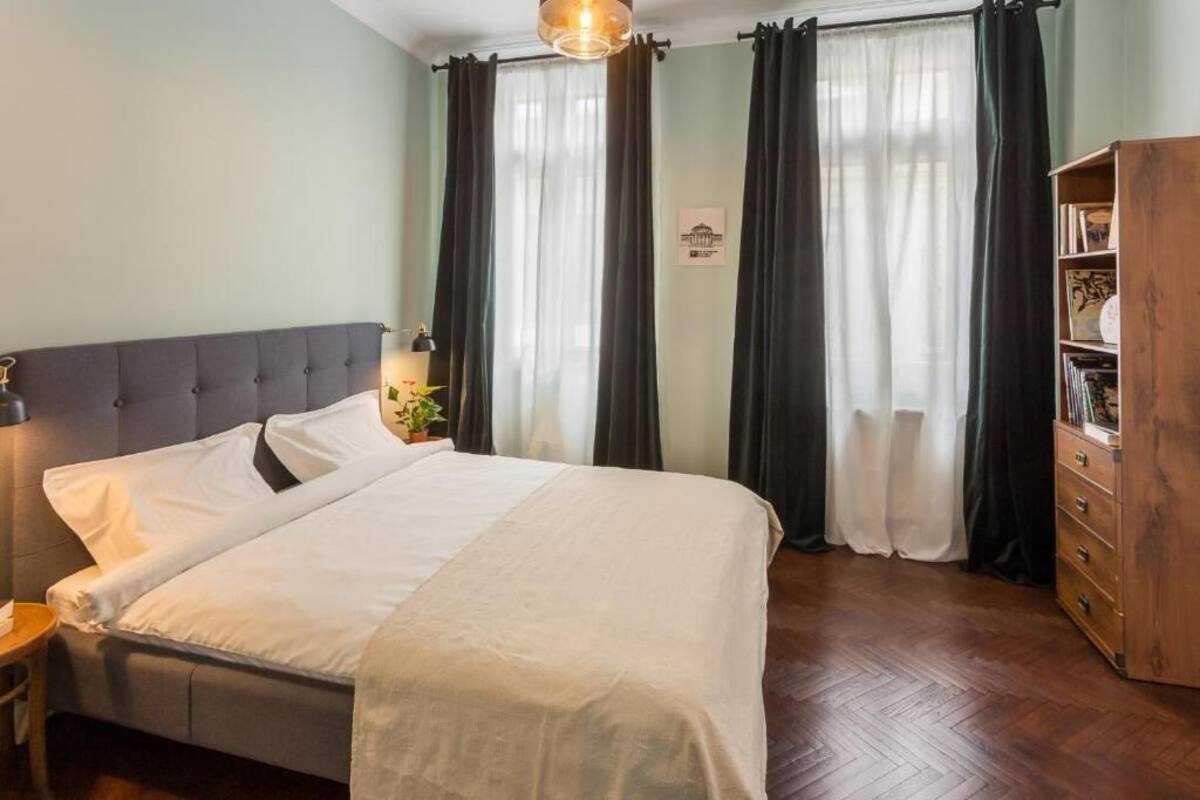 A neatly made bed with a grey headboard, a wooden nightstand with a lamp, and a wooden dresser with a mirror.