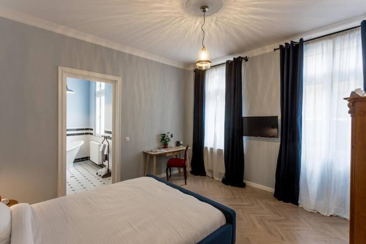 A hotel room with a bed, a desk, a chair, a TV, and a bathroom visible through an open door.