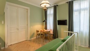 Une pièce avec un canapé vert, une table à manger avec des chaises, une rambarde blanche et un téléviseur fixé au mur.