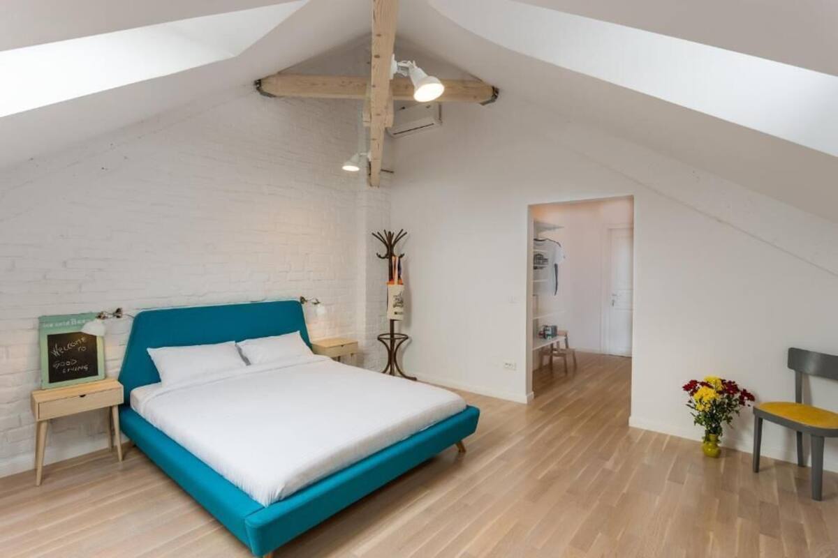 A bedroom with a bed, a nightstand, a chair, a vase with flowers, and a door leading to another room.