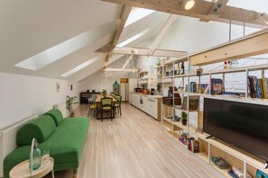Een modern loft appartement met een eethoek, een groene bank, een televisie en een boekenkast.