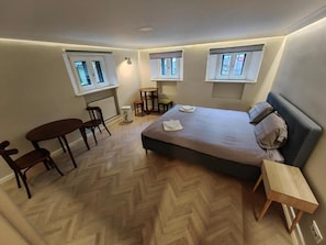 A bedroom with a bed, a small table, two chairs, a radiator, and three windows. - Little Bucharest Mansion  (Bucharest)