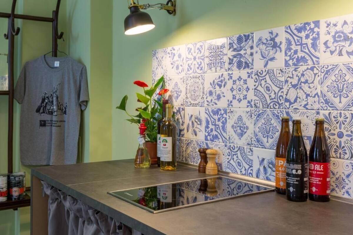 A kitchen counter with a tiled backsplash, a hanging t-shirt, and three bottles of beer.