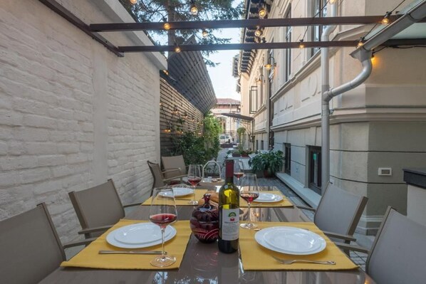 Een terras met eettafels voor twee personen, elk met een fles wijn en glazen.