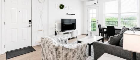 A modern living room with a sofa, a television, and a dining area with a table and chairs.
