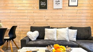 Un espacio de sala acogedor con un sofá gris oscuro, un cojín con forma de corazón, y una mesa con frutero, croissant y taza de café.
