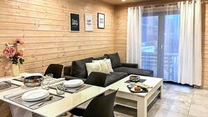 Una habitación acogedora con pared de madera, un sofá, una mesa de comedor con platos y vasos, y una ventana con cortinas.