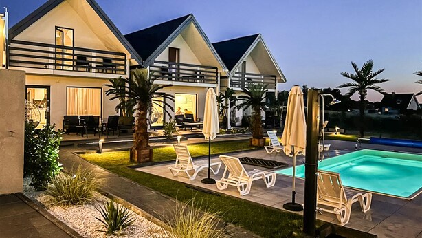 Una casa moderna de dos pisos con piscina, mobiliario exterior y un patio bien iluminado.