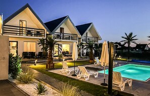 A modern two-story house with a swimming pool, outdoor seating, and a well-lit patio area.